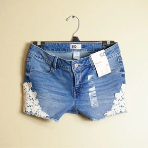 Juniors' SO® Mid-Rise Shortie Shorts with embroidered flower patch.